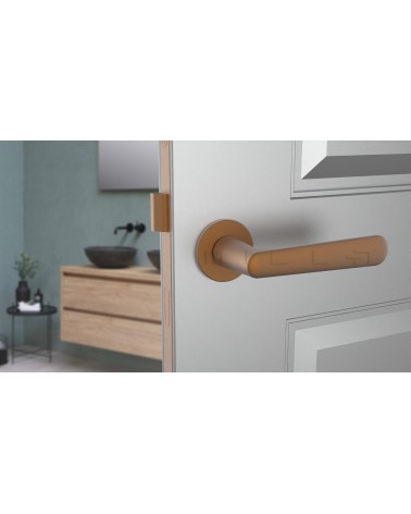 Poignée de porte cuivre ARIA poignée design vue de face montée sur une porte entrouverte