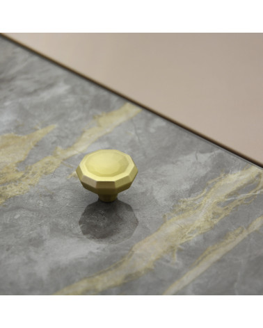 Bouton de meuble or mat CAMPANA poignée design posé sur une surface plane avec un fond texturé