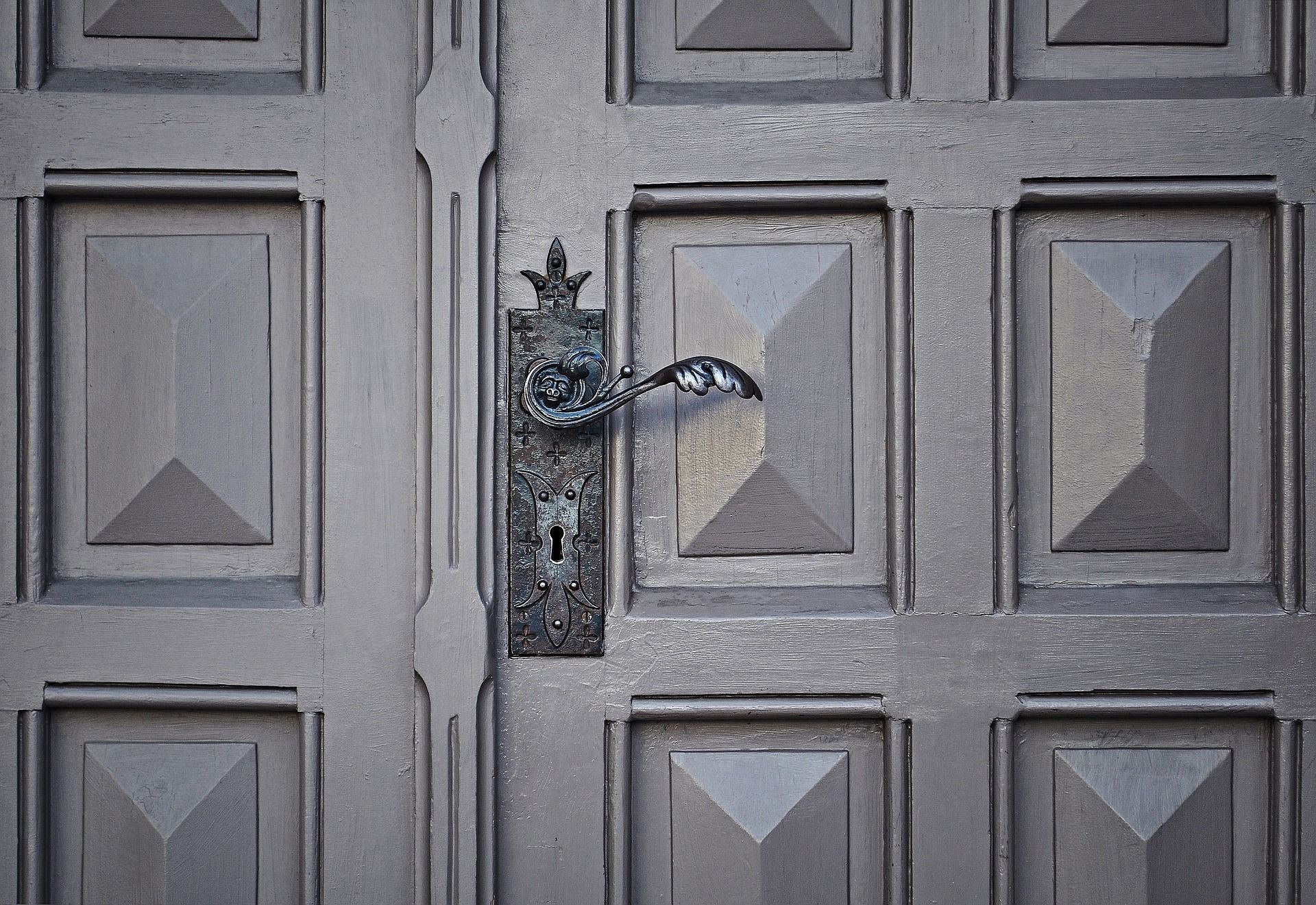 Poignée de porte noire posée sur une porte exterieure de couleur grise