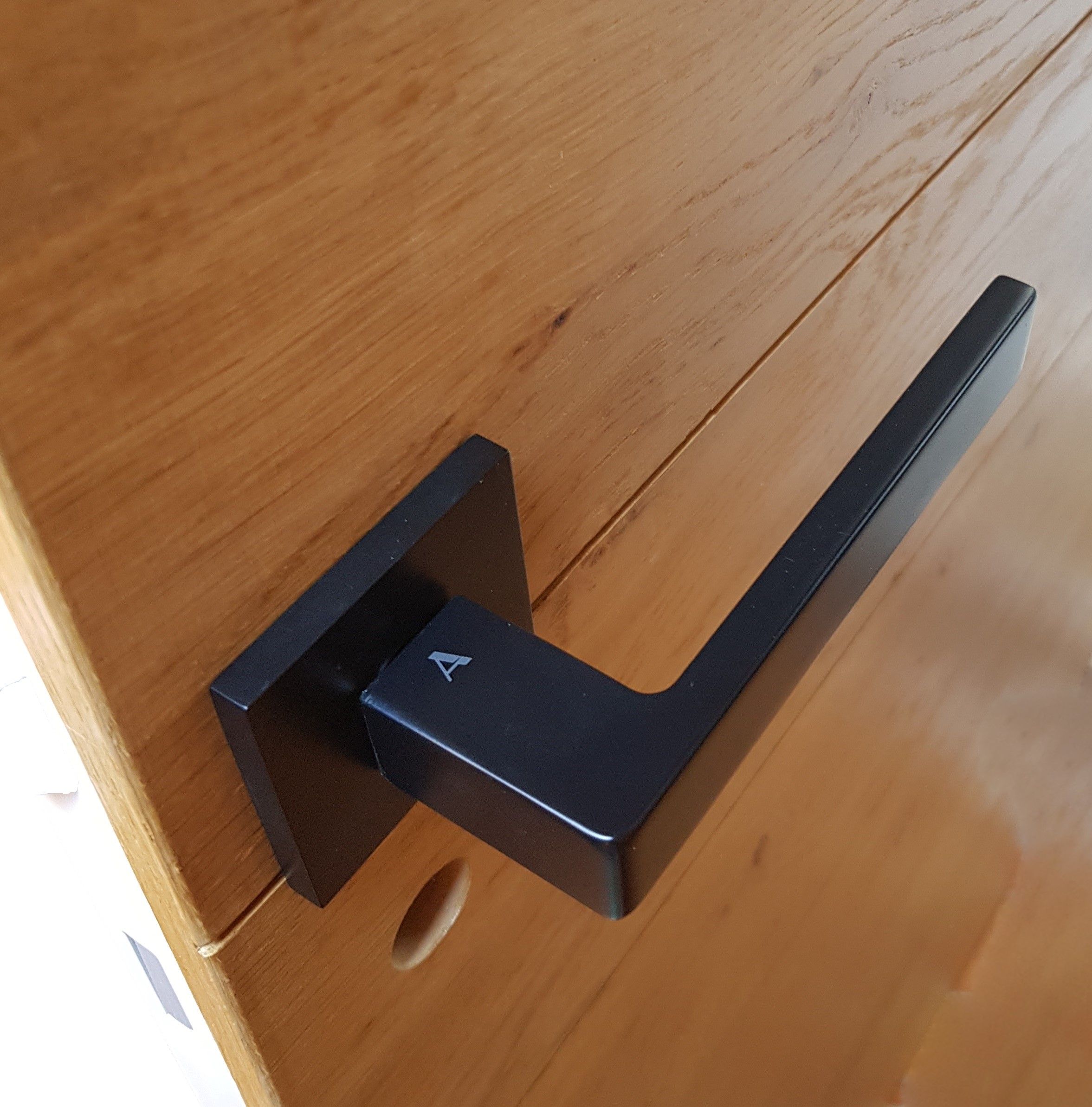 poignée de porte intérieure noire sur une base carré posée sur une porte en bois